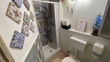 A bathroom with patterned tiles, a shower, a toilet, a sink with a soap dispenser, and a towel rack.
