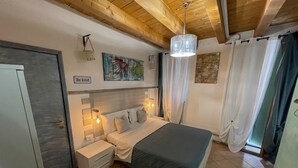 A bedroom with a bed, bedside tables, a nightstand, a wall-mounted lamp, a ceiling fan, and a door. - Vicolo 22 (Verona)