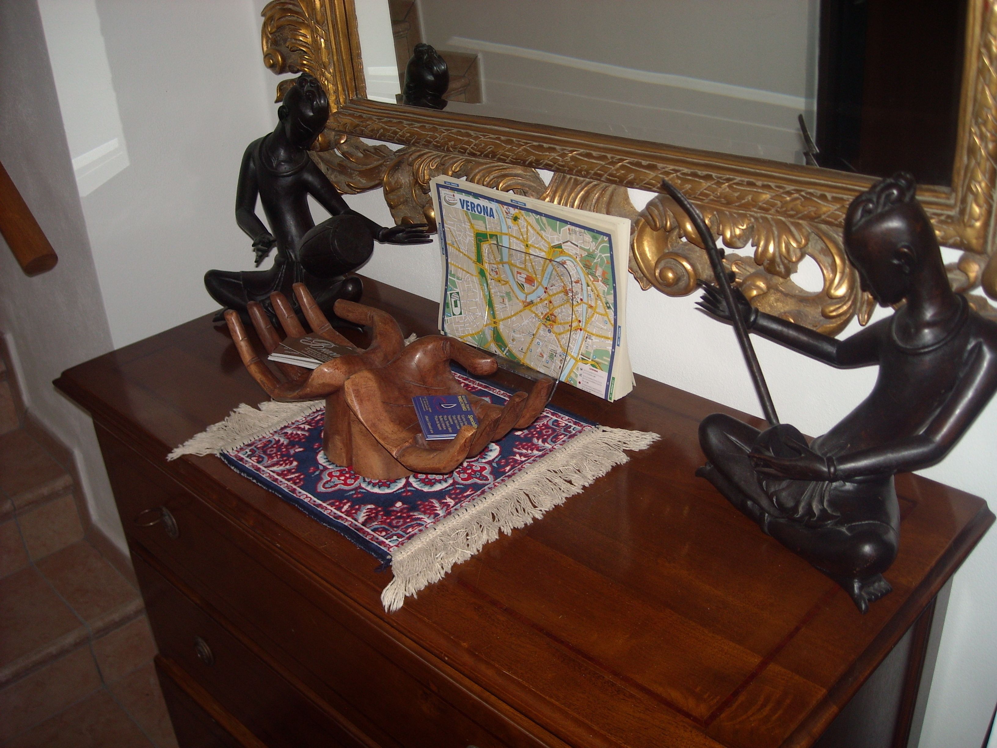 Un aparador de madera con una escultura decorativa de madera, un mapa y un espejo con detalles en oro ornamentado.