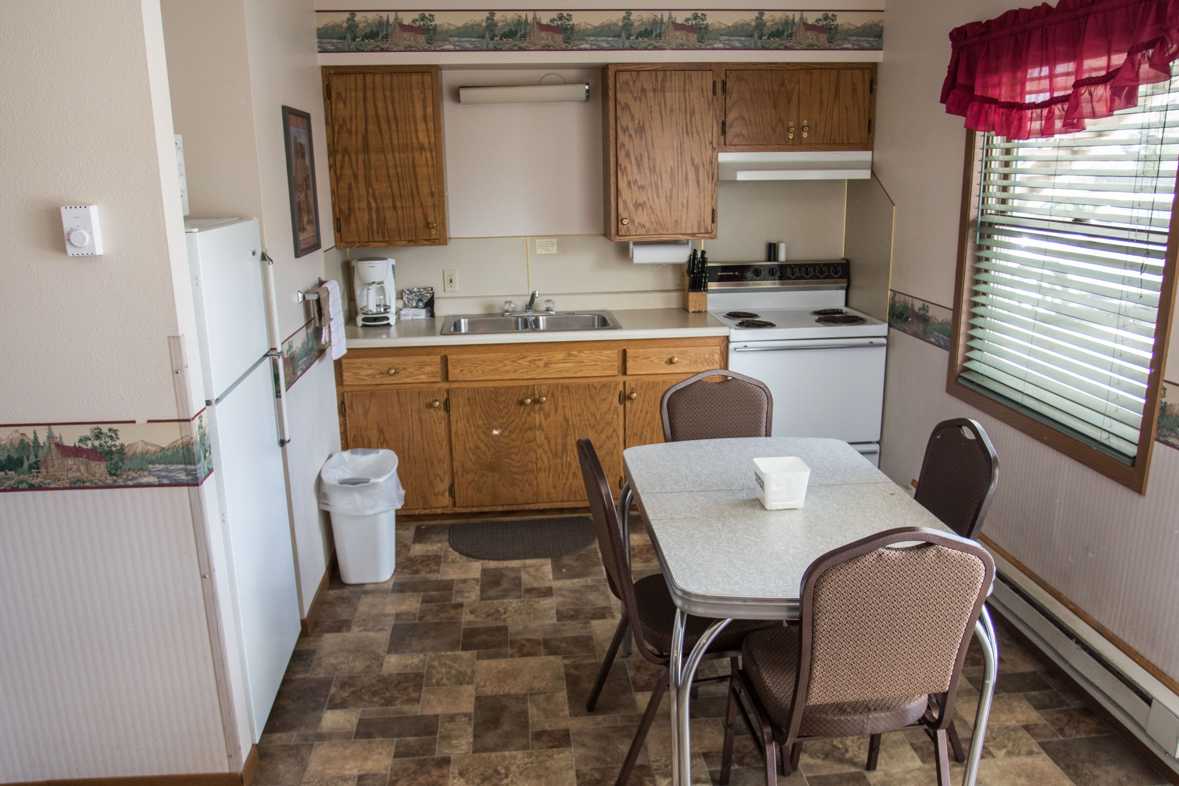 Une cuisine de taille réduite, dotée de meubles en bois, d’un réfrigérateur blanc, d’une cuisinière et d’une table à manger avec des chaises.