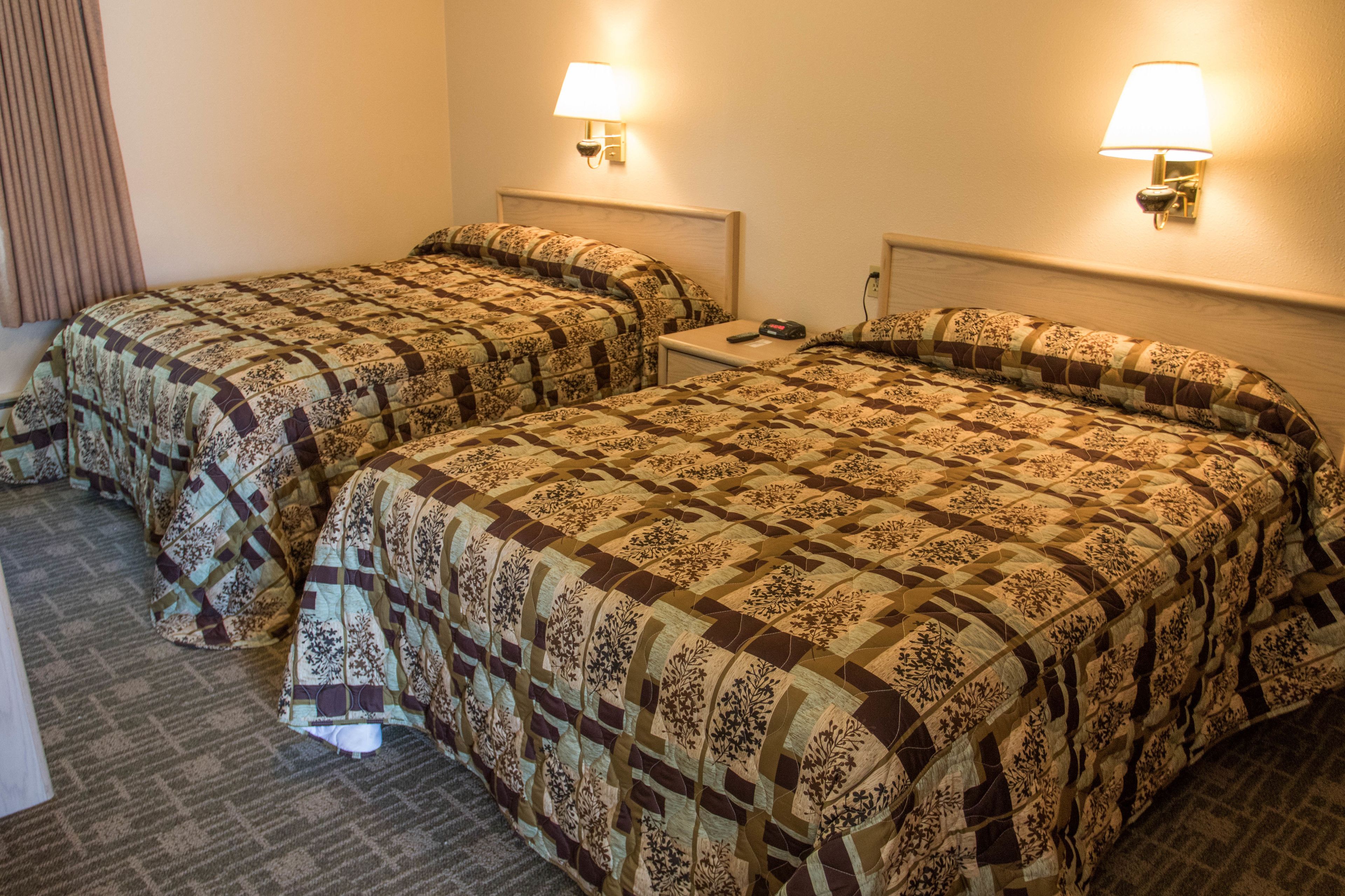 Ein Hotelzimmer mit zwei Betten, jeweils mit einem gemusterten Überwurf, Nachttischlampen und einem kleinen Tisch dazwischen.