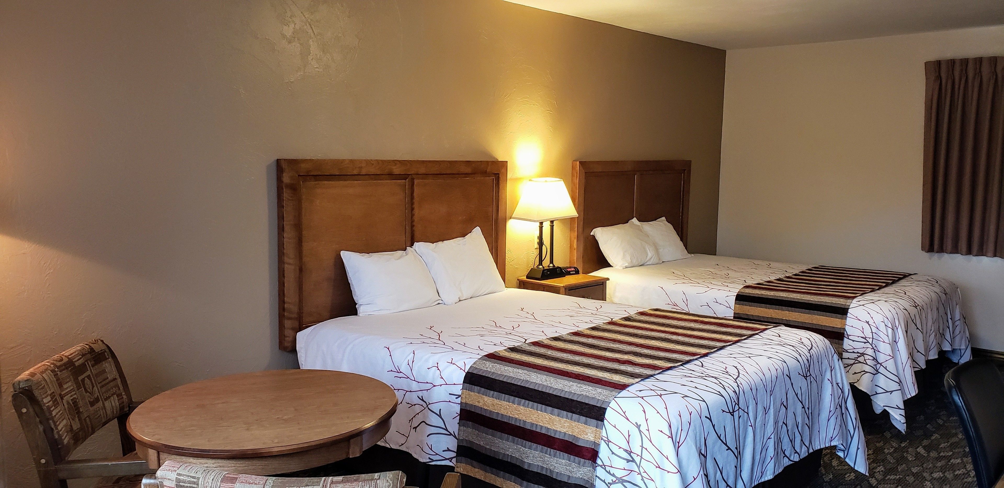 Habitación de hotel con dos camas, una mesita redonda pequeña, una silla y una lámpara.