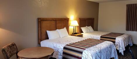 Habitación de hotel con dos camas, una mesita redonda pequeña, una silla y una lámpara.
