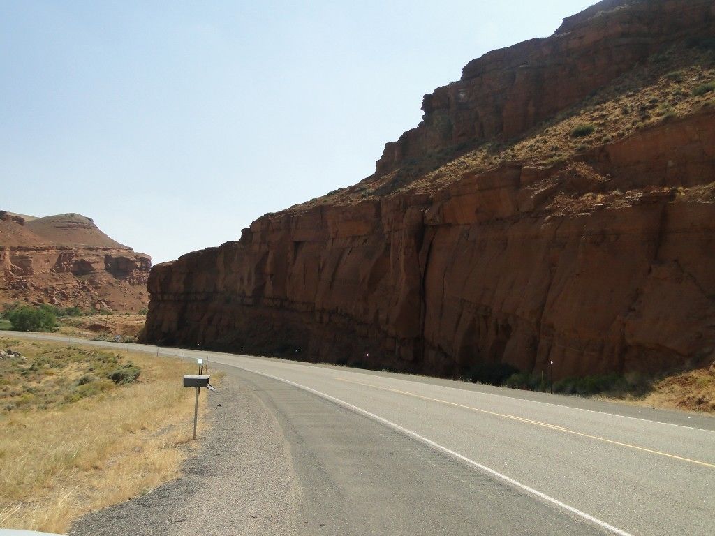 A road with a mailbox on the side, surrounded by red rock formations.