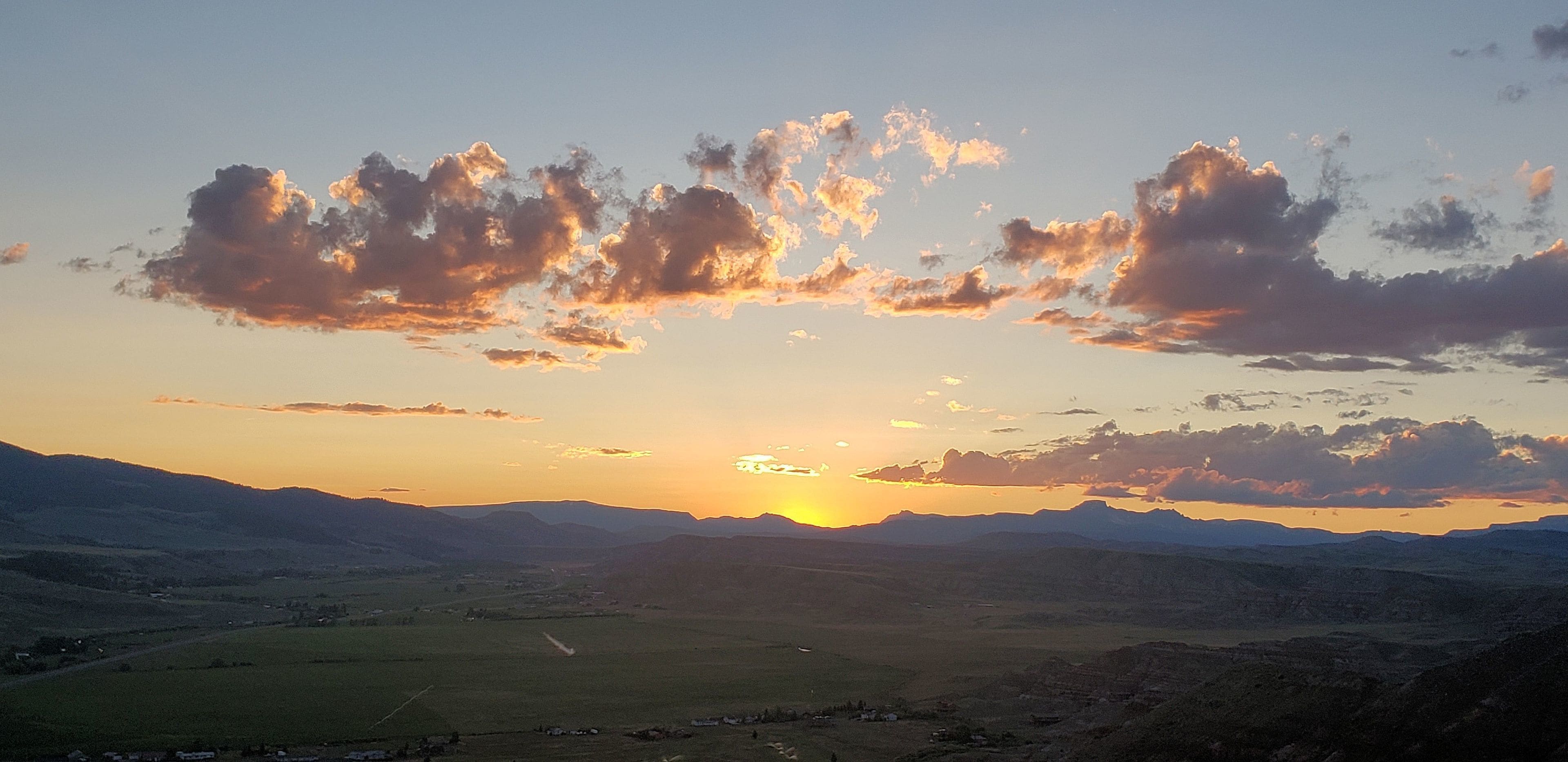 A sunset over a valley with scattered clouds and distant mountains.