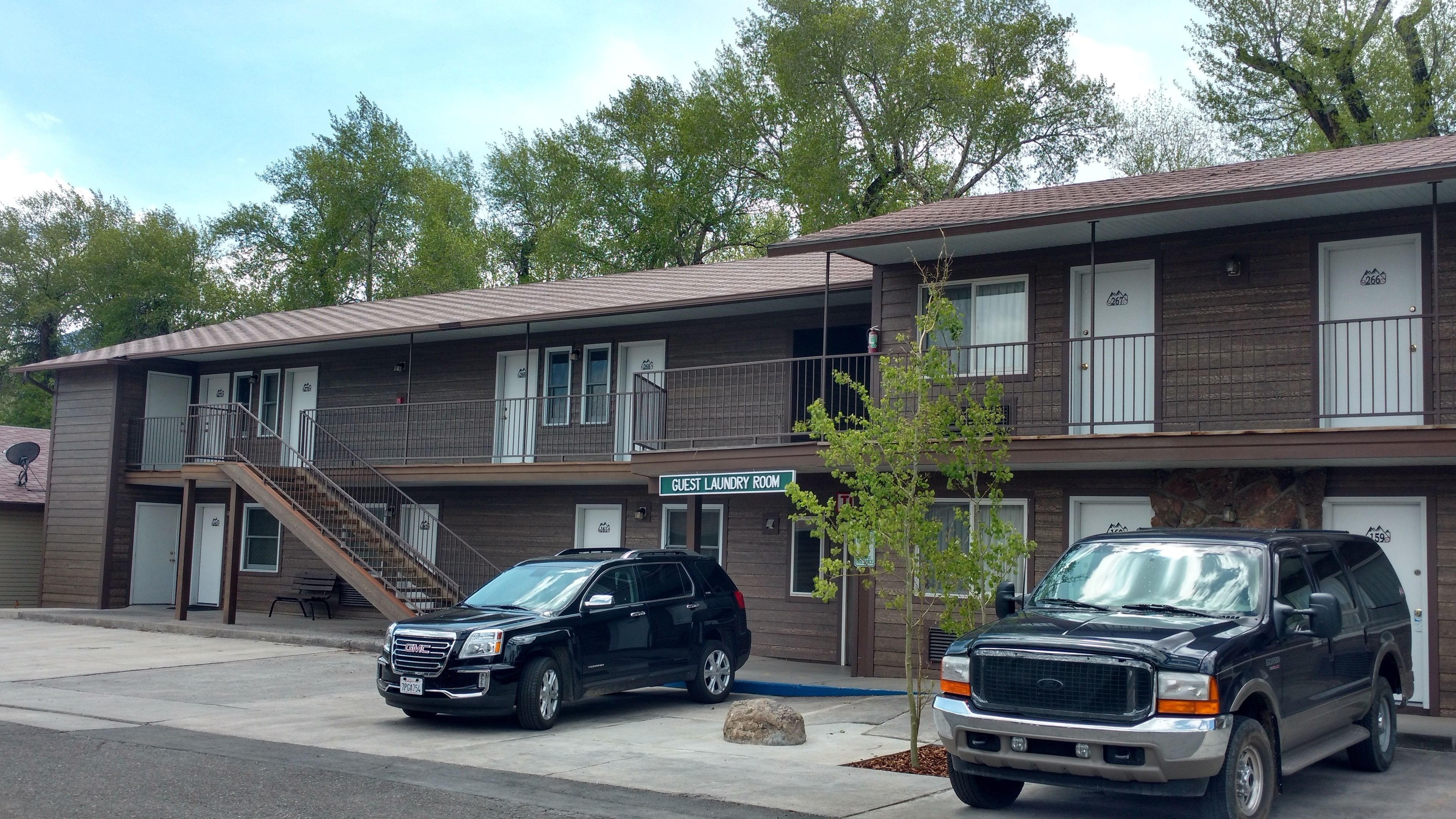 A two-story motel with a guest laundry room sign, a satellite dish, and two parked SUVs.