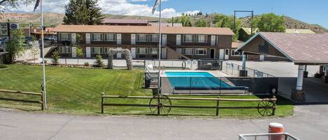 A hotel with a swimming pool, a fenced area, and a mountain backdrop.