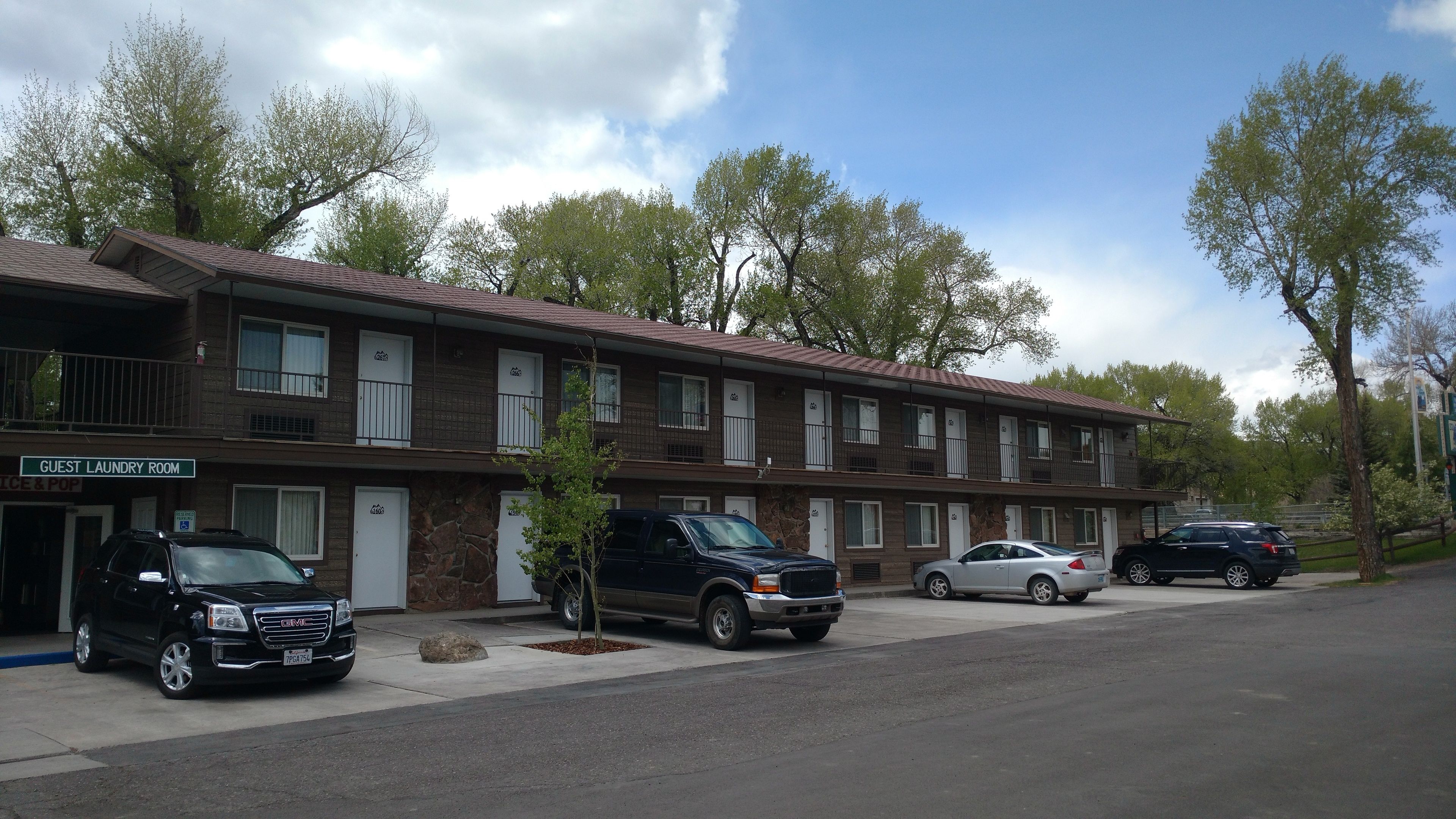 A multi-story motel with a guest laundry room, several vehicles parked in front, and a clear sky.