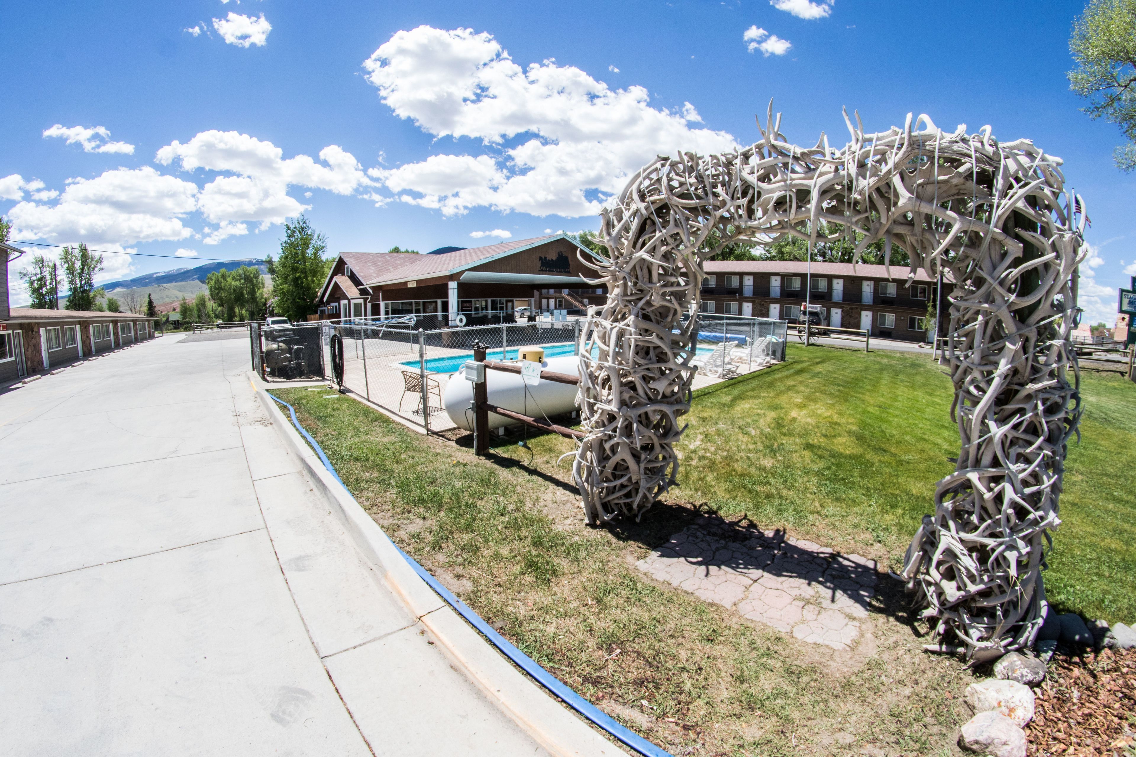 A modern hotel with a pool, a unique metal sculpture, and a clear view of the mountains in the background.