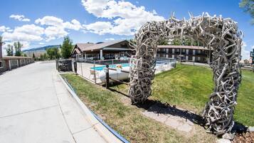 A modern hotel with a pool, a unique metal sculpture, and a clear view of the mountains in the background.
