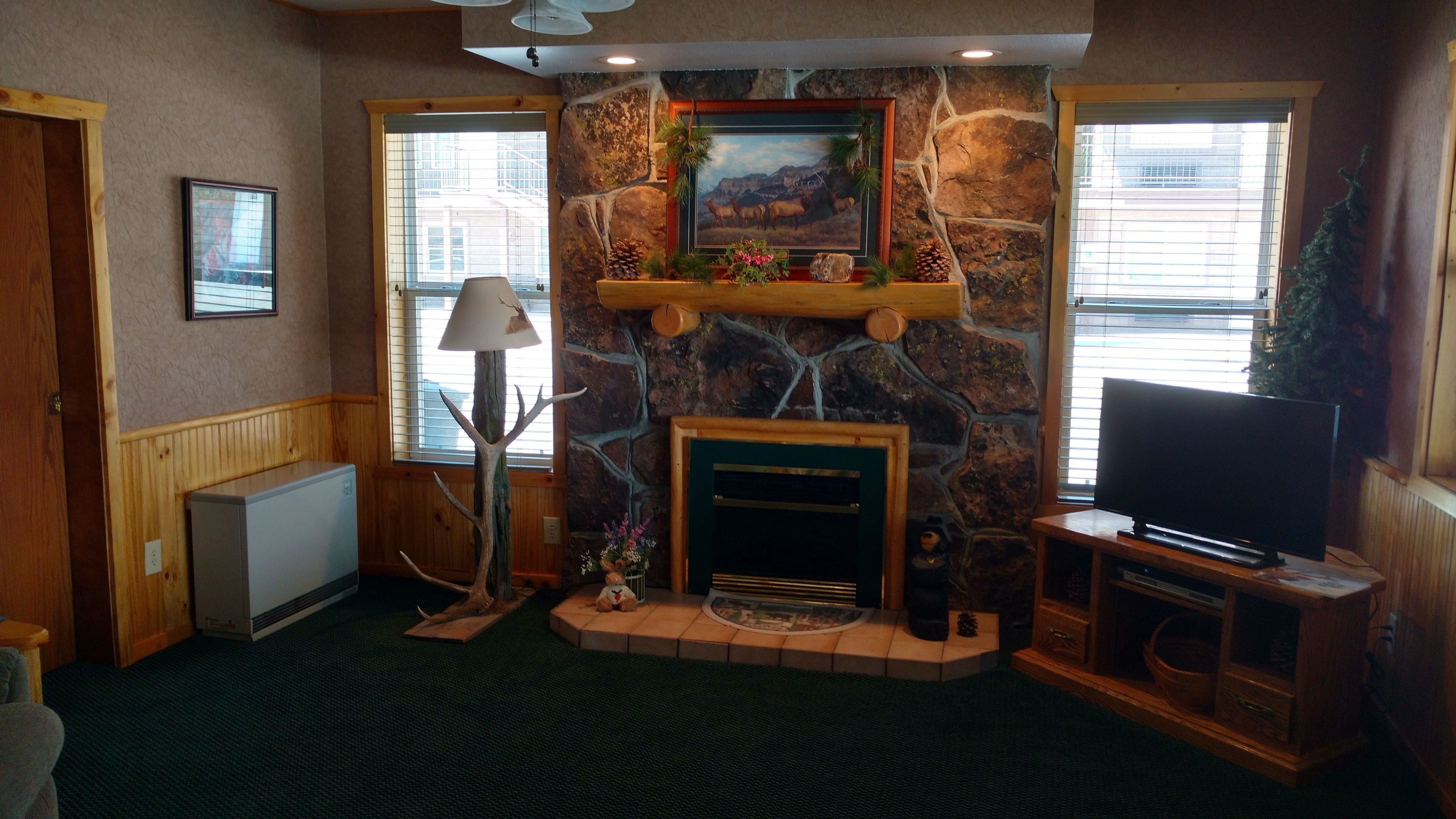 A cozy living room with a stone fireplace, a television, and a decorative tree.