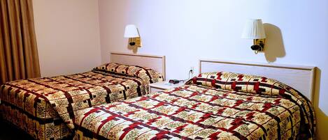 Una camera d'albergo con due letti, ognuno con una coperta a motivi e un comodino, e due lampade a parete.