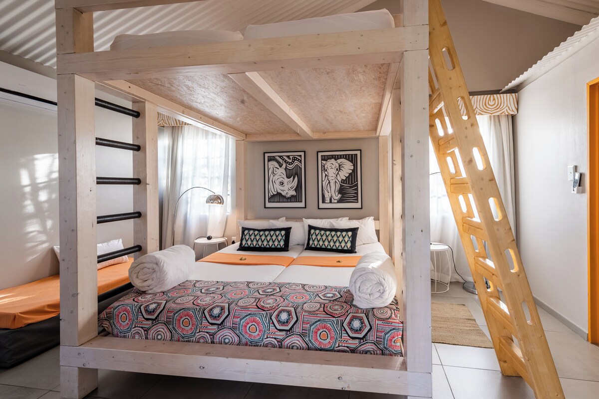 Un lit recouvert d’une couvre-lit à motifs, une échelle en bois et deux tableaux encadrés accrochés au mur.