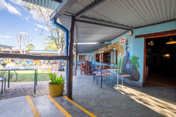An outdoor seating area with tables and chairs, a potted plant, and a mural on the wall.
