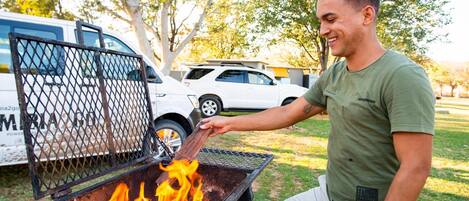 A person grilling outdoors with a vehicle in the background.