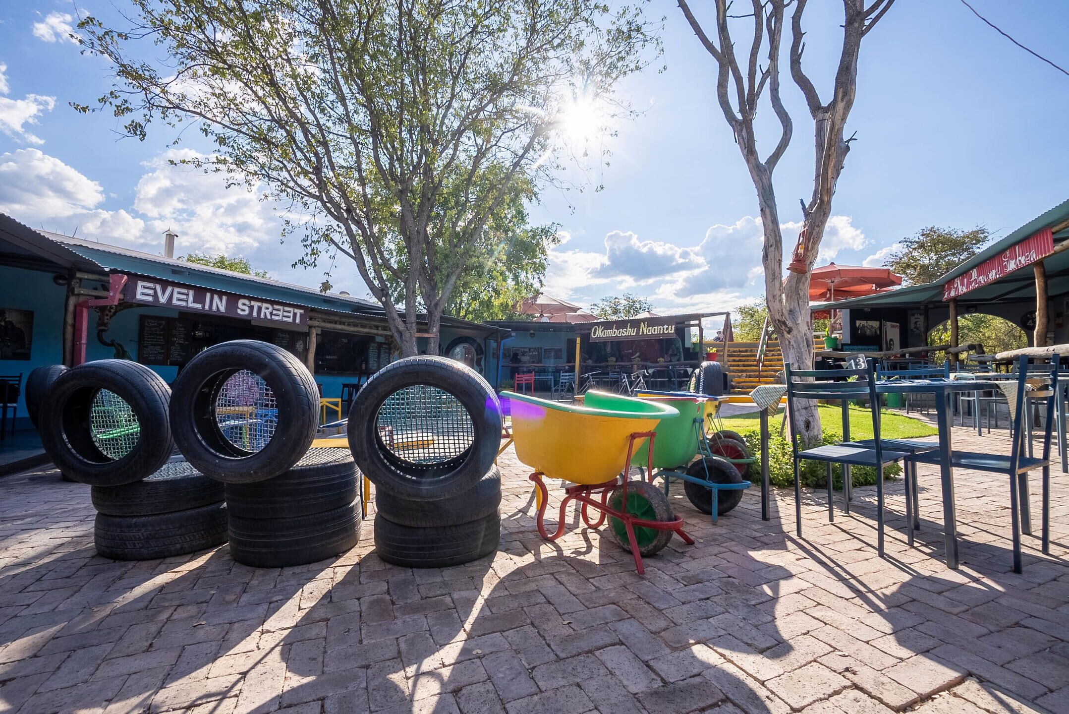 A paved outdoor area with tires and a wheelbarrow, a building labeled 'Evelin Street,' and a sign for 'Okambashi Naantu.'
