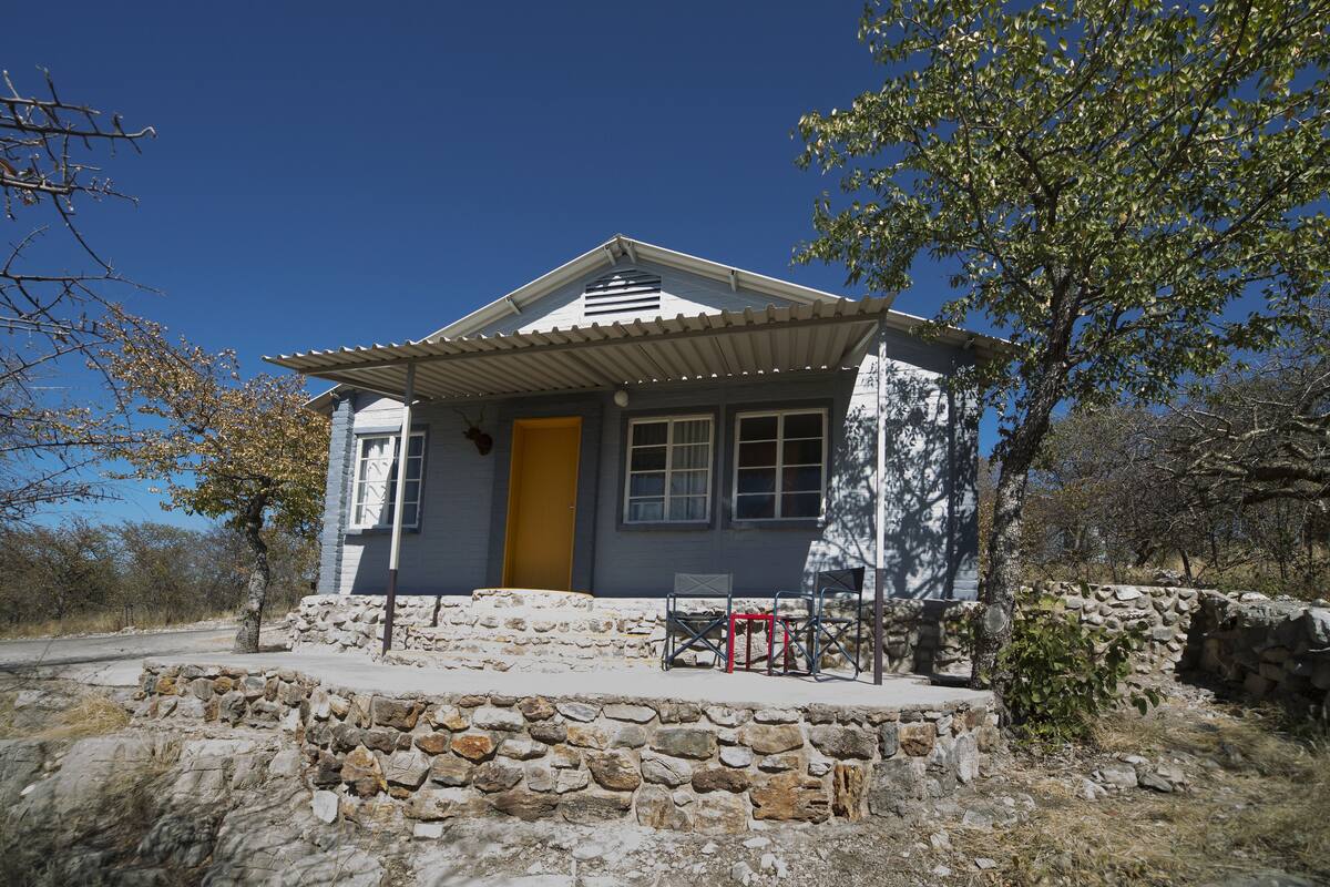 Uma casa com base de pedra, porta amarela e pequena varanda com uma cadeira.