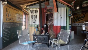 Un intérieur rustique à l’esthétique rétro, avec une affiche « VOTEZ UDF », une table en bois, deux chaises en osier et une pancarte « BIENVENUE » accrochée à un meuble.
