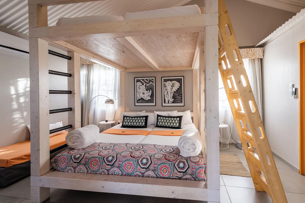 Uma cama com colcha estampada, uma escada de madeira e duas molduras na parede.