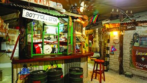 Un bar à l’ambiance rétro, avec une enseigne indiquant « BOTTLOR STORE » et « UPINGTON 1445 km ». On peut y voir des fûts de bière et un tabouret.