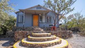 Une maison avec un escalier en pierre menant à une porte en bois, entourée d’arbres et d’un mur de pierre.