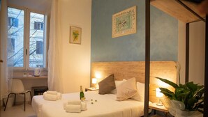 A hotel room with a bed, a desk, a chair, a window, and a plant. - Romerooms (Rome)