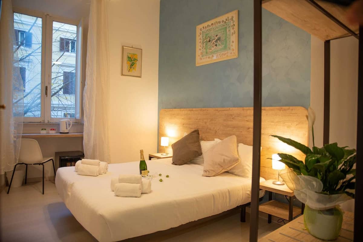 Habitación de hotel con cama, escritorio, silla, ventana y planta.