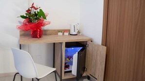 A compact kitchenette with a wooden countertop, a white chair, a small fridge, and a decorative red plant. - Romerooms (Rome)