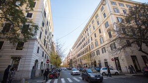 A street view with buildings, parked cars, and pedestrians. - Romerooms (Rome)