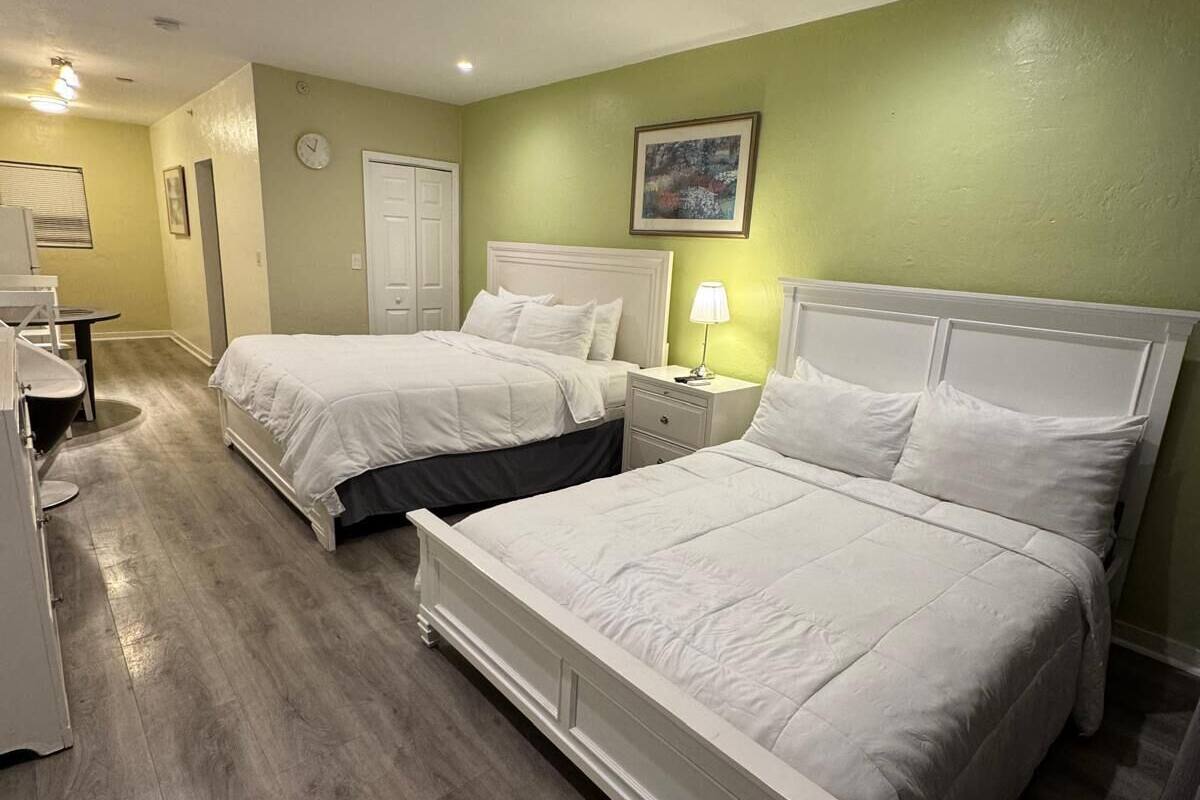 A hotel room with two beds, a desk, a chair, a lamp, and a clock on the wall.