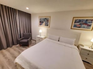 Ein Hotelzimmer mit einem großen Bett, einem Sessel, zwei Nachttischen mit Lampen und Vorhängen.