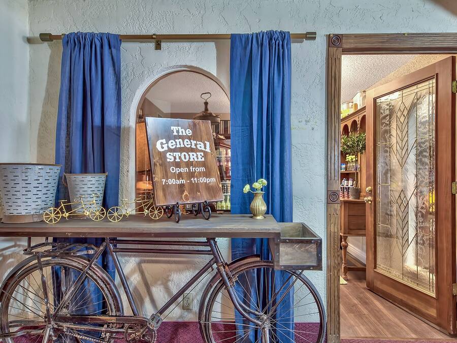 Un vélo d’époque, une enseigne indiquant « The General Store » et précisant les heures d’ouverture (de 7 h 00 à 23 h 00), et une porte en bois avec un panneau de verre.