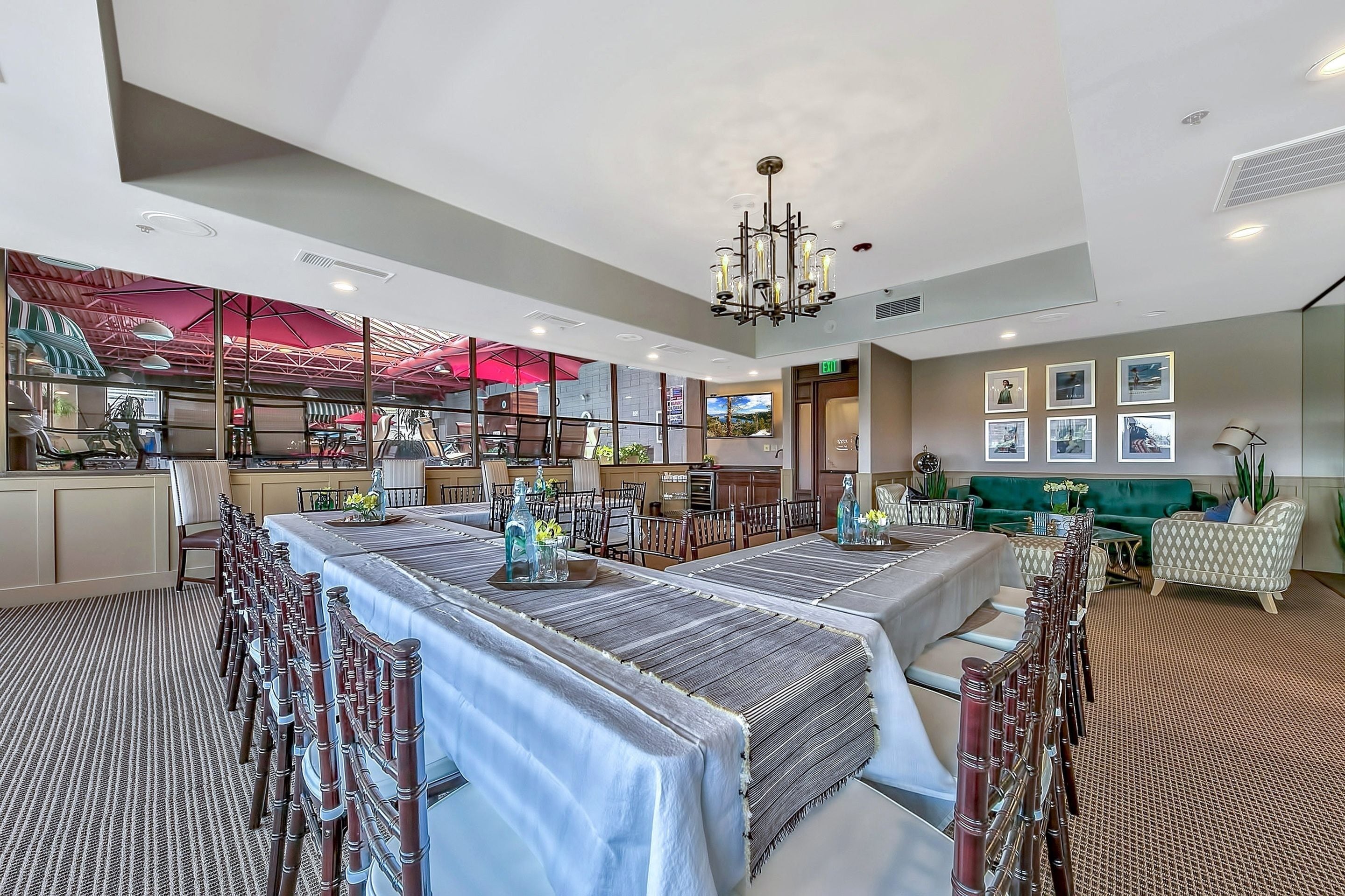A spacious dining area with long tables and chairs, a chandelier, and a green sofa in the background.