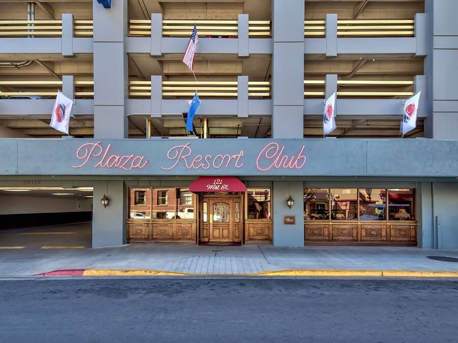Exterior del Plaza Resort Club, con una entrada destacada, un toldo rojo y varias banderas.