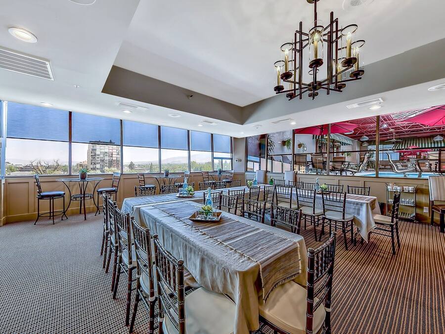 Un comedor amplio con techos altos y ventanas grandes que ofrecen vista a la ciudad. Las mesas están dispuestas con sillas, y un candelabro cuelga del techo.