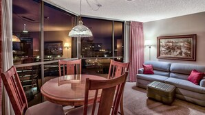 A modern living room with a dining area, large windows with city views, a sofa, and a framed artwork on the wall. - Plaza Resort Club (Reno)