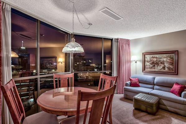 Una sala de estar moderna con comedor, ventanas amplias con vistas a la ciudad, un sofá y una obra de arte enmarcada en la pared.
