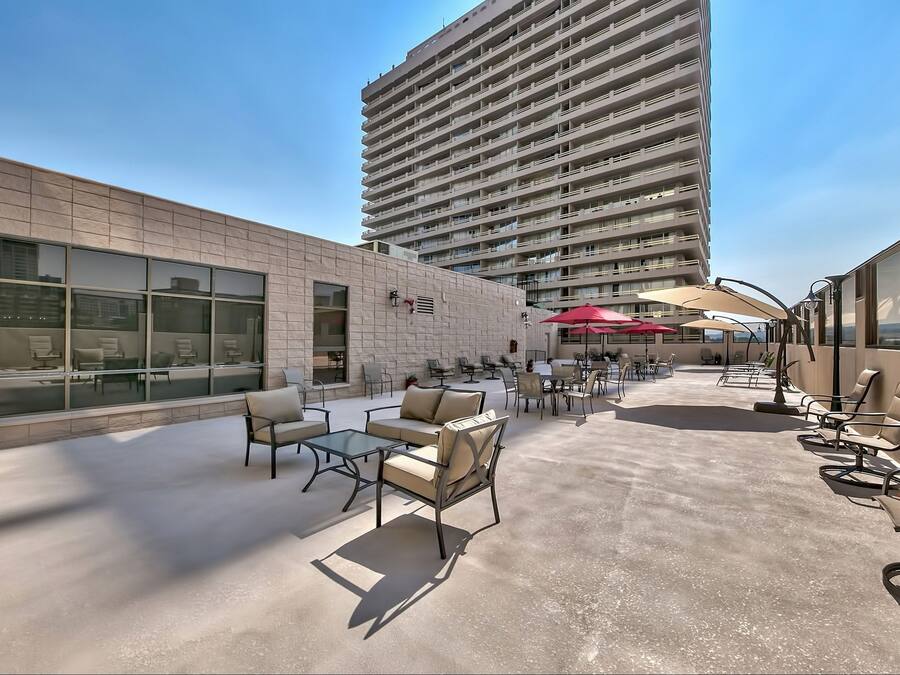 An outdoor patio with seating and tables, a tall building in the background, and a clear sky.