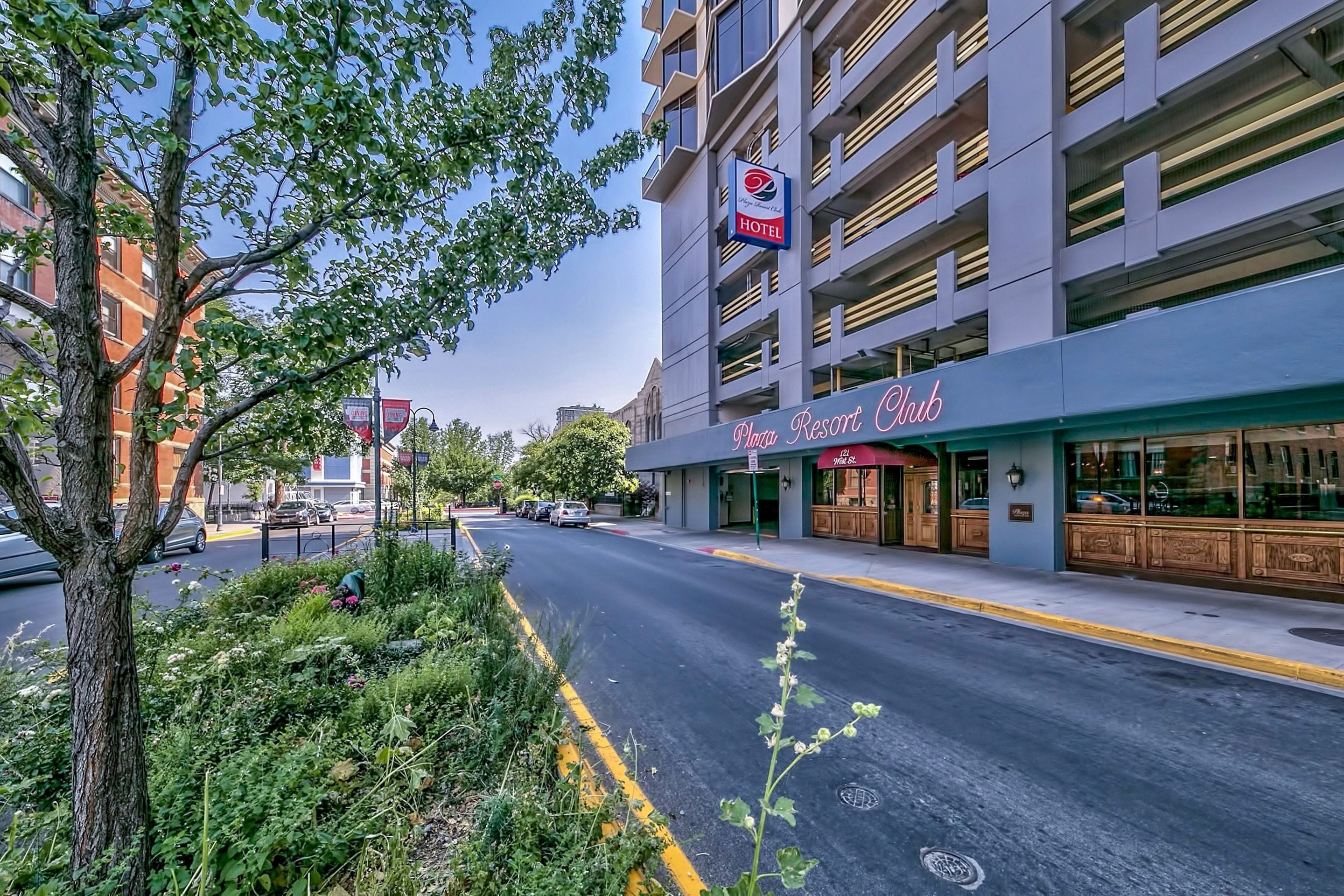 A hotel with a modern facade, a visible sign for the "Plaza Resort Club," and a street with parked cars and greenery.