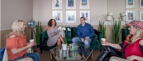 A group of people sitting on a green sofa and chairs in a well-lit room with framed pictures on the wall.