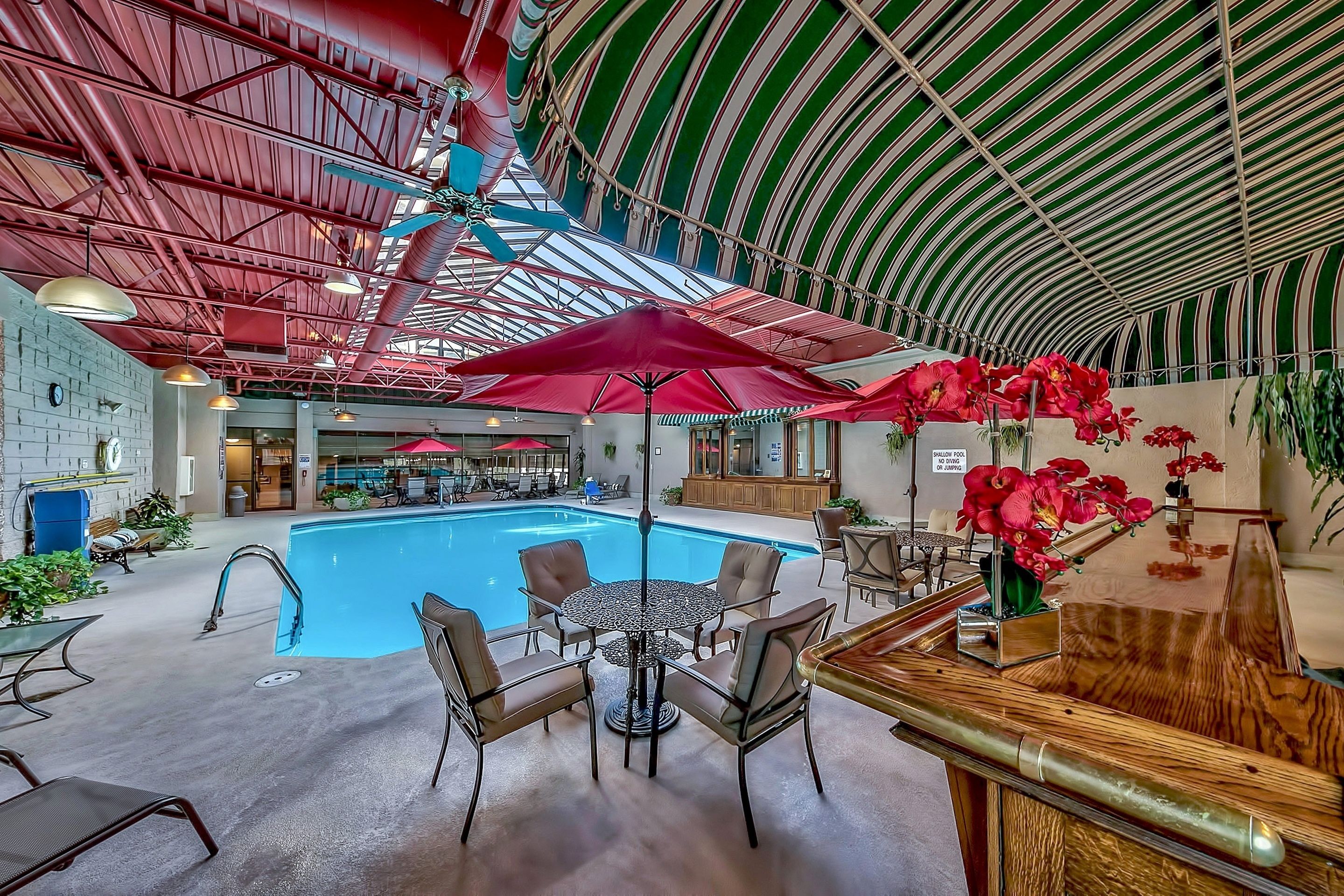 An indoor swimming pool area with a bar, seating, and red umbrellas.