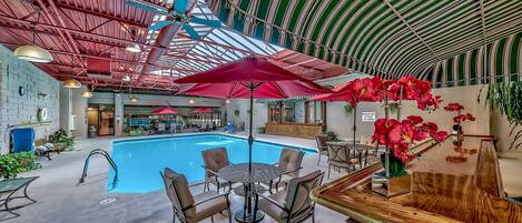 An indoor swimming pool area with a bar, seating, and red umbrellas.