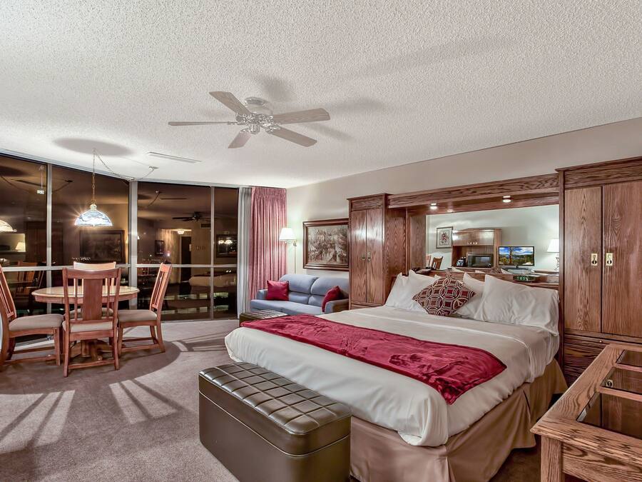 A hotel room with a bed, a desk, a chair, a sofa, a TV, and a ceiling fan.