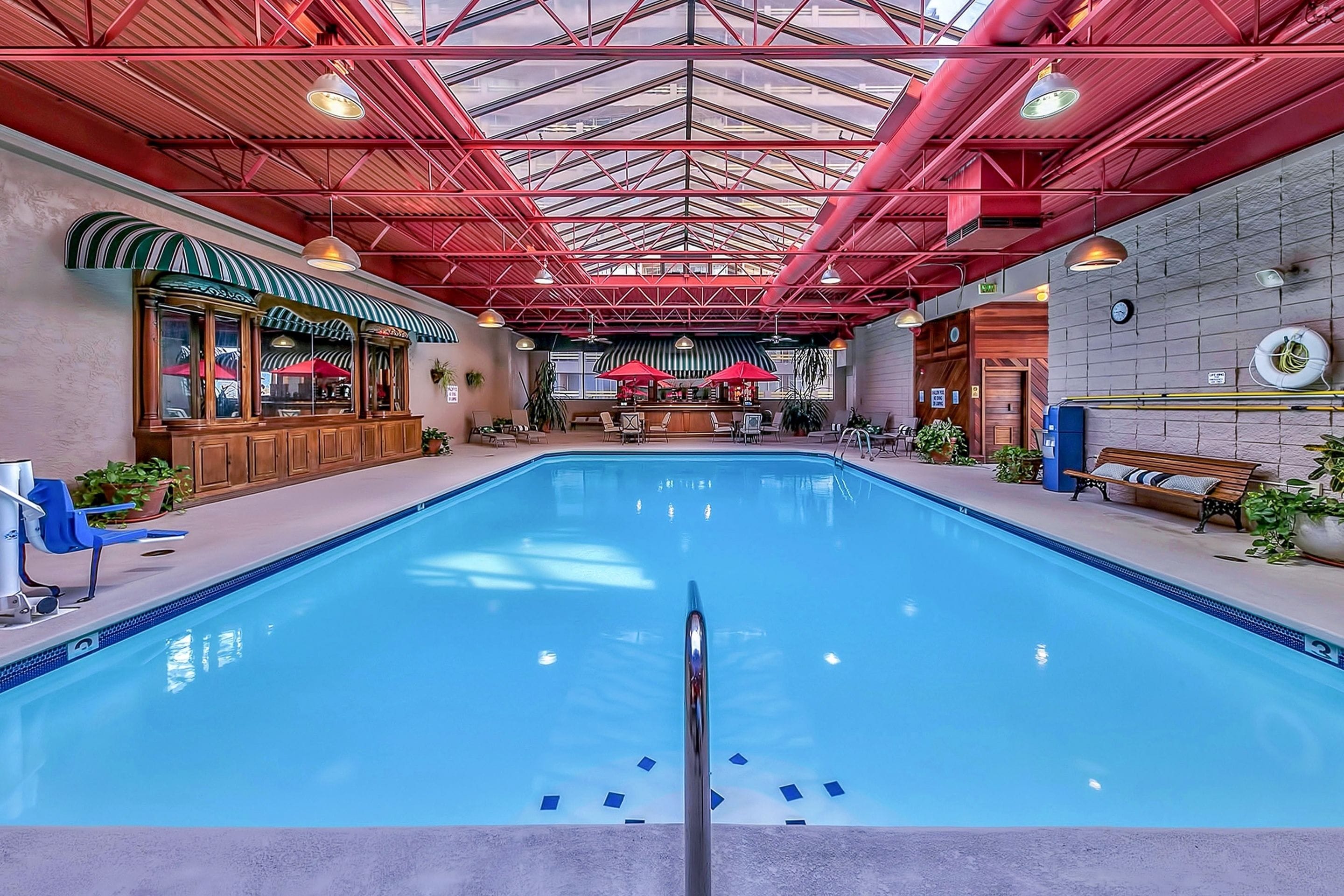 An indoor swimming pool with a clear view of the bar area, lounge chairs, and a high ceiling with red beams.