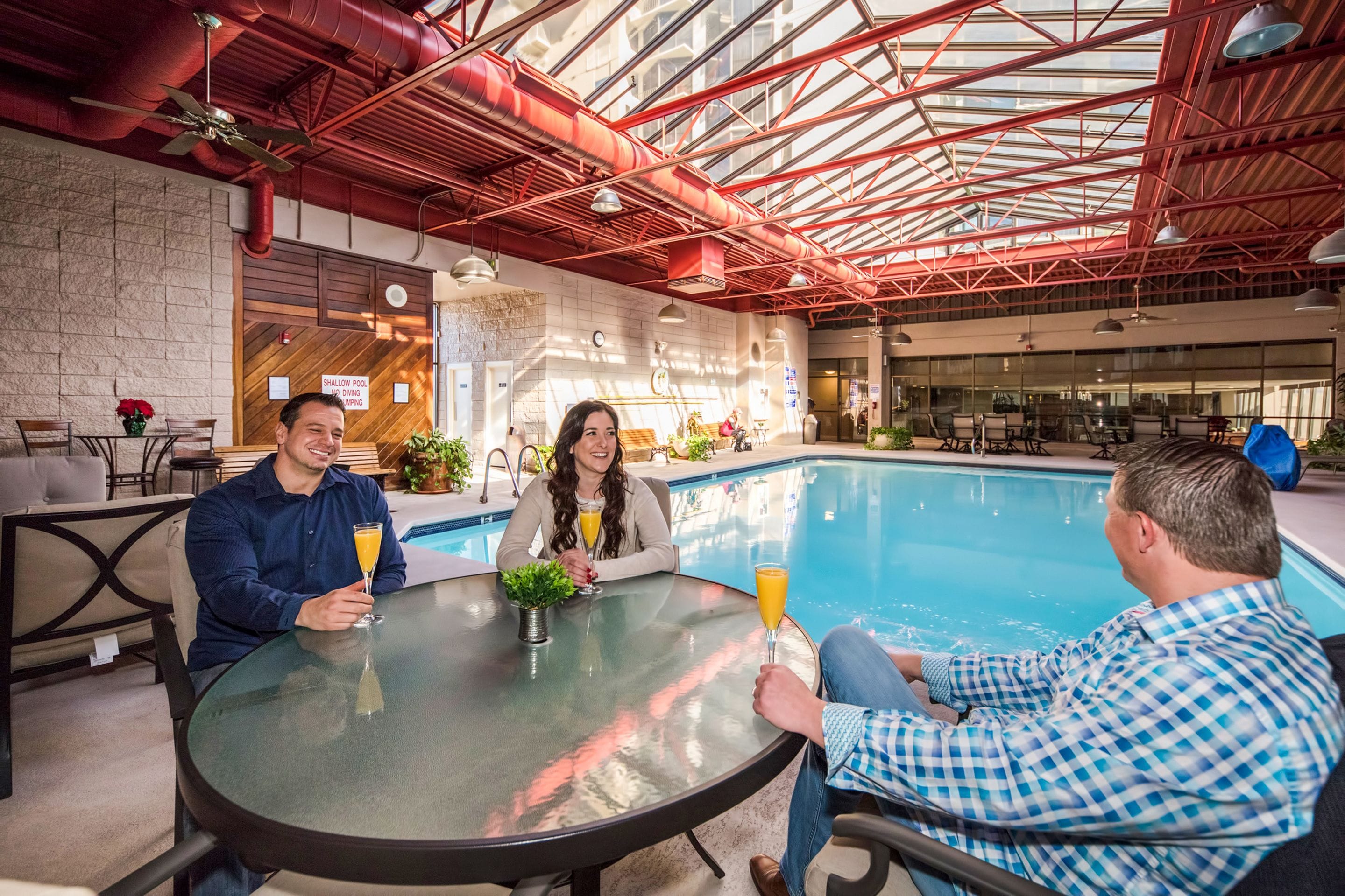 Un espace piscine intérieur avec une table en verre, des chaises et un plafond orné de poutres rouges.