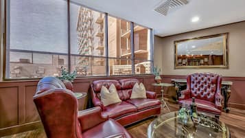 A spacious living area with a leather sofa, armchairs, and a glass coffee table. Large windows provide a view of the cityscape.