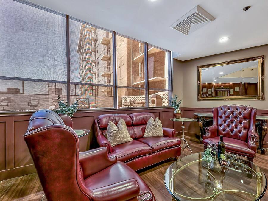 A spacious living area with a leather sofa, armchairs, and a glass coffee table. Large windows provide a view of the cityscape.