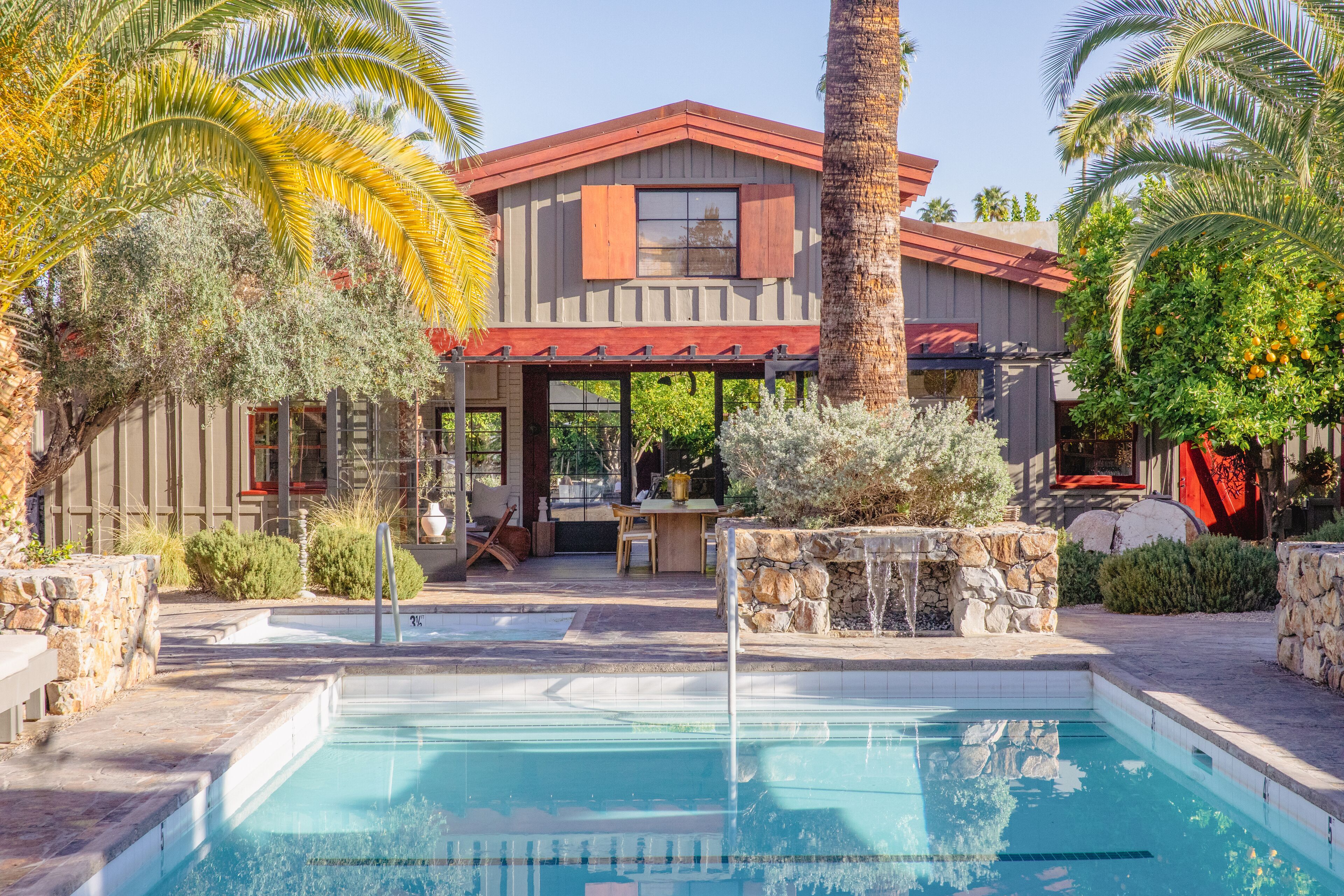 A pool area with a house, stone walls, and palm trees.