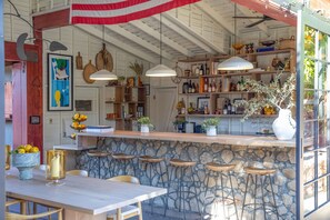 A rustic kitchen with stone countertops, wooden stools, and hanging pendant lights.
