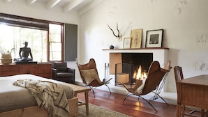 A cozy bedroom with a large bed, two leather chairs, a fireplace, and a statue. - Sparrows Lodge (Palm Springs)